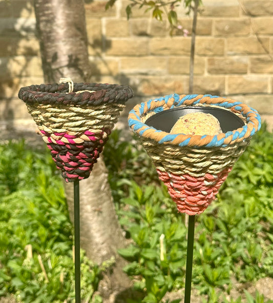 bird feeders made of munja grass and cotton rope, displayed on garden stakes in a backyard setting