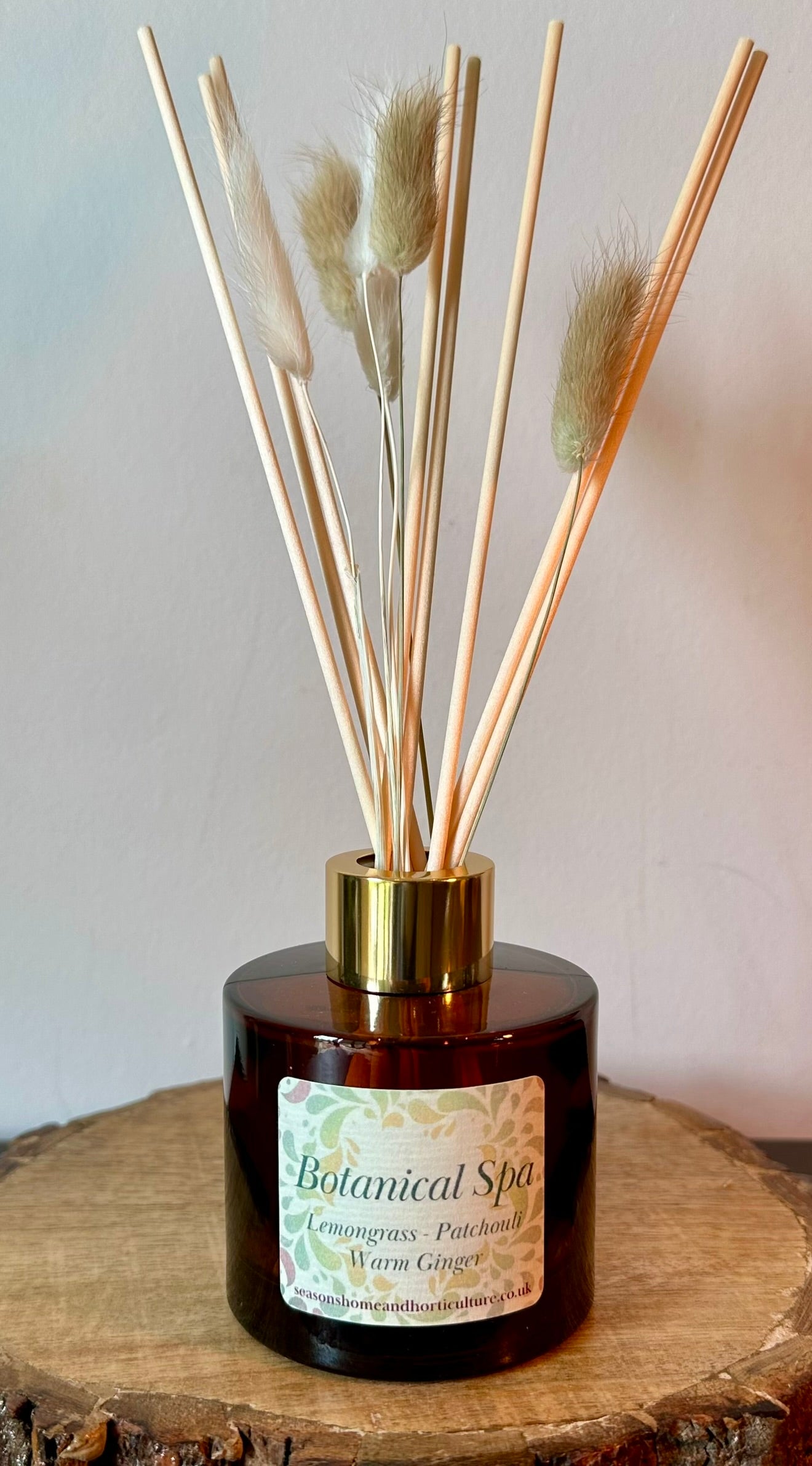 Botanical Spa reed diffuser with lemongrass, patchouli and warm ginger fragrance in amber glass bottle with natural reeds on wooden surface