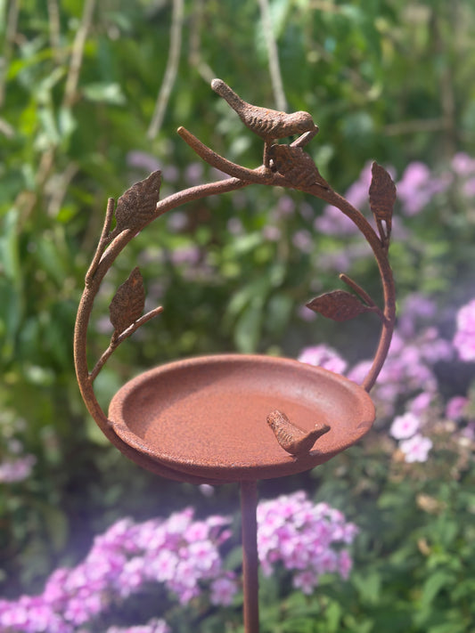 Decorative garden stake birdbath with metal bowl for wild birds in a flower garden setting