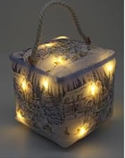 A square fabric doorstop with a rope handle, featuring a winter Christmas scene print with Santa, snowmen, and a snowy house. An inset in the top-left shows the bag illuminated with warm lights.