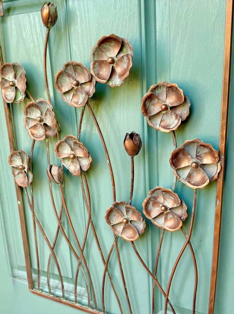 Metal cornflower wall art mounted on outdoor wall adding botanical charm to garden spaces