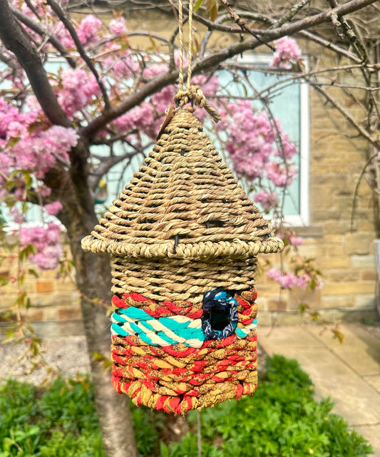 handwoven bird feeders made of munja grass and cotton rope, displayed on garden stakes in a backyard setting
