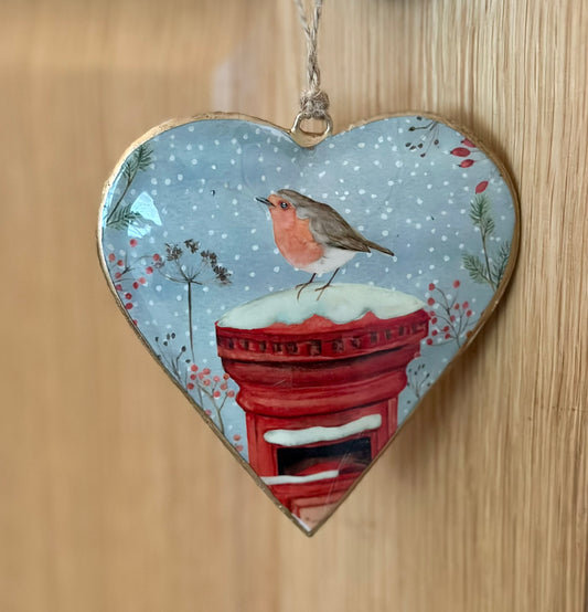 Heart-shaped metal ornament with a robin and postbox design on a wooden background