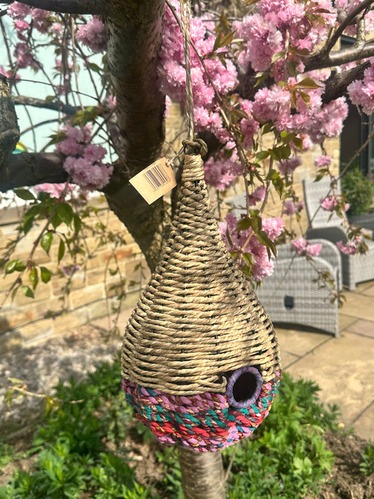 a teardrop shaped bird feeder made of munja grass and cotton rope, displayed on garden stakes in a backyard setting