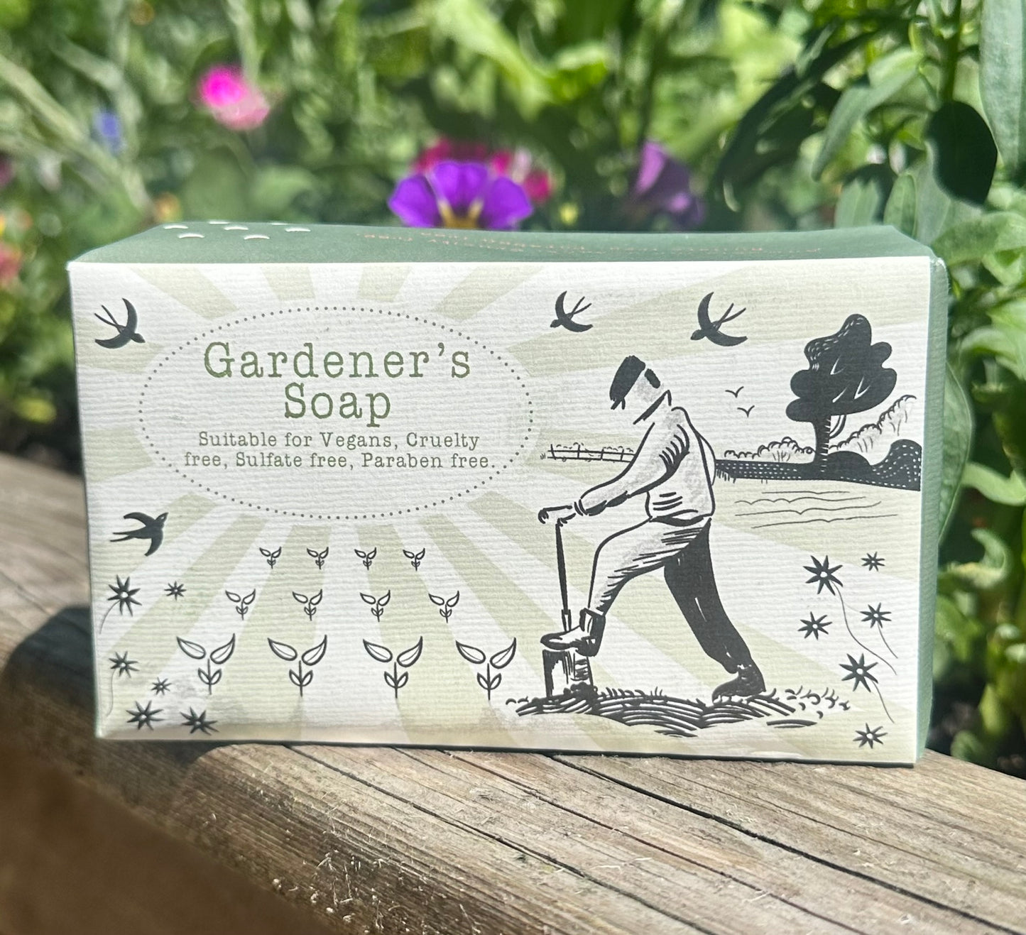 Natural Gardener’s Soap photographed in garden setting with colourful pansies and fresh herbs behind