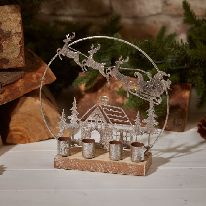 Decorative Christmas scene four taper candle holder with Santa, reindeer sleigh, house, and trees on a wooden base.