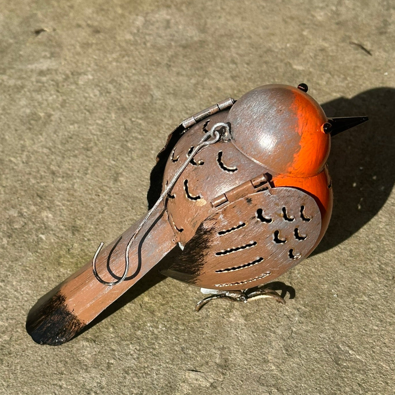 Decorative bird ornament with orange head and brown body on a concrete surface