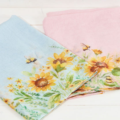 Floral fabric with sunflowers and bees on a light blue and pink background