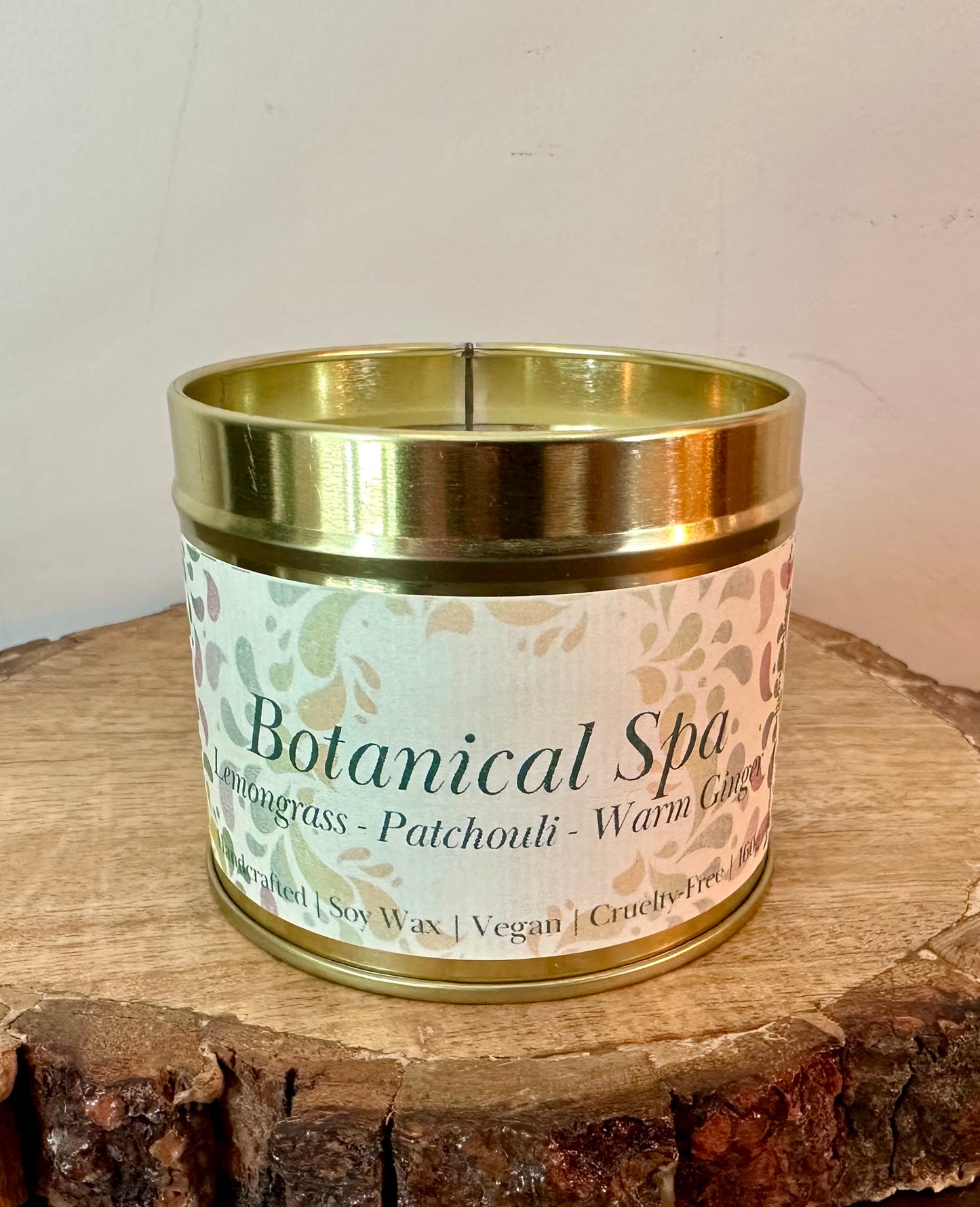 Botanical Spa soy candle with lemongrass, patchouli and warm ginger scent in gold tin on wooden surface