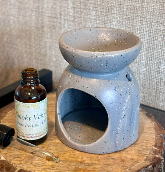 Speckled blue ceramic oil burner with a bottle of Smoky Velvet perfume oil on a wooden surface.