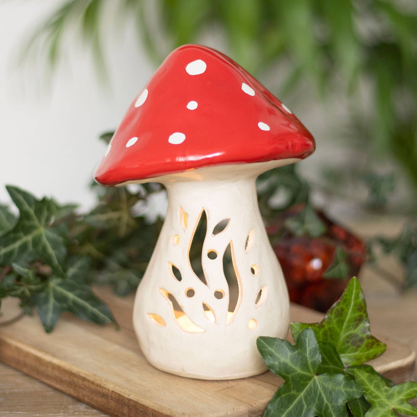 Mushroom-shaped lantern with red cap and white spots on a wooden surface with green leaves.