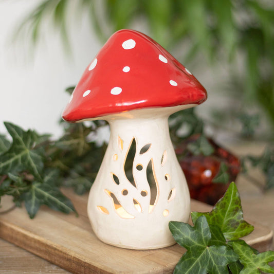 Mushroom-shaped lantern with red cap and white spots on a wooden surface with green leaves.