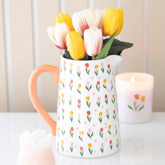 White pitcher with floral pattern filled with tulips on a white surface.