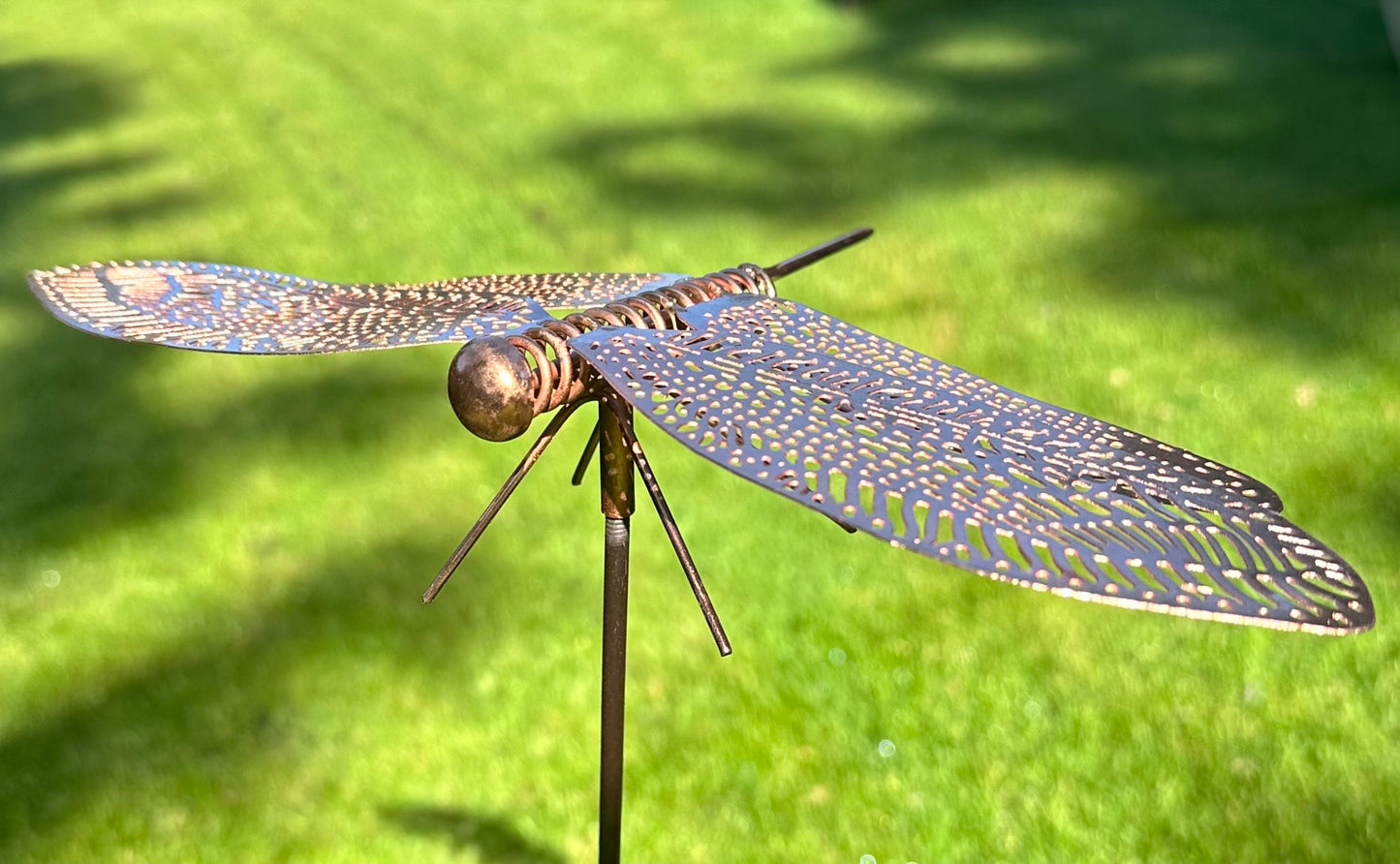 Metal dragonfly plant stake with intricate copper wings for garden borders and landscaped outdoor spaces