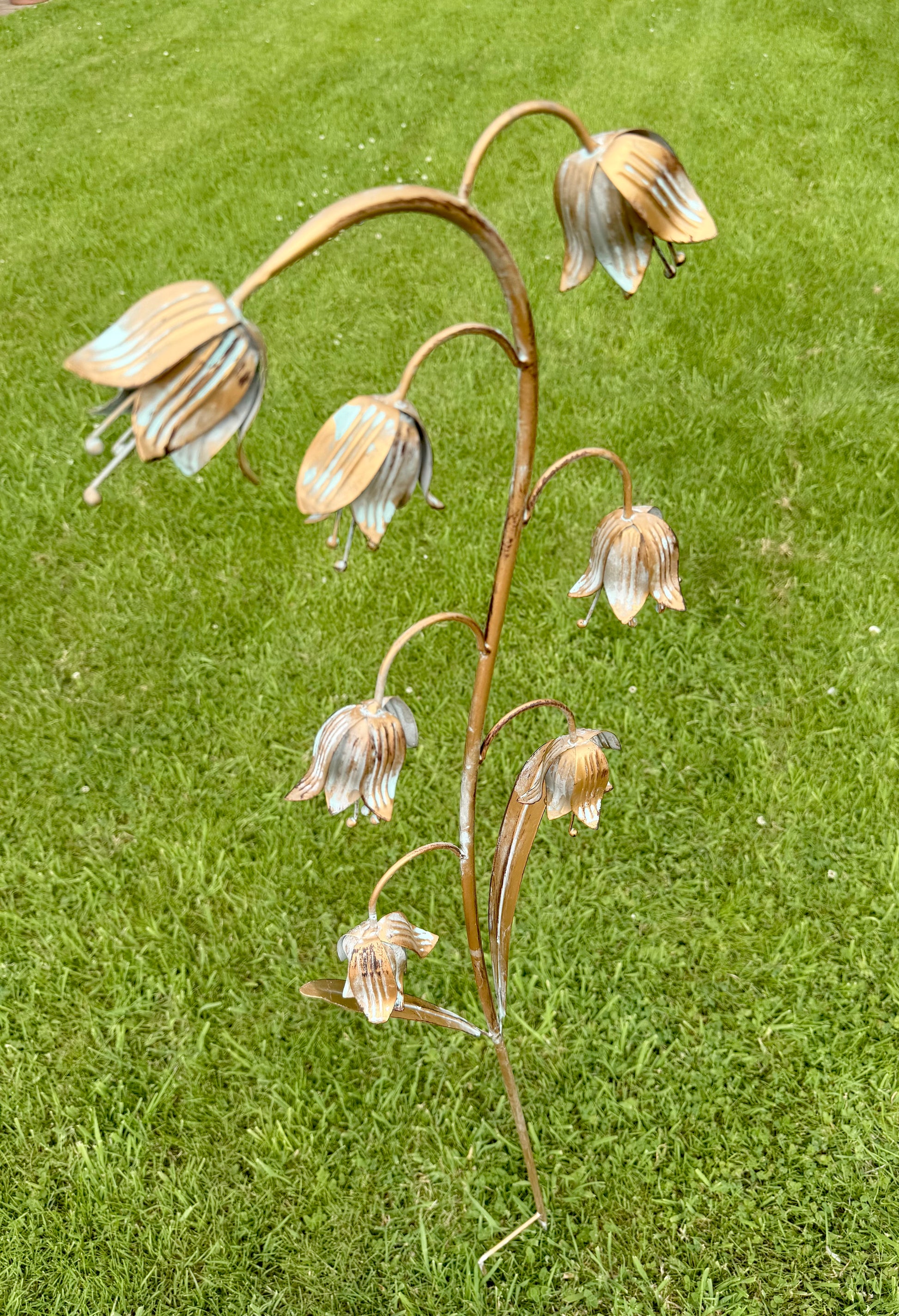 Weathered metal fritillaria ornament displayed among plants in a cottage garden setting
