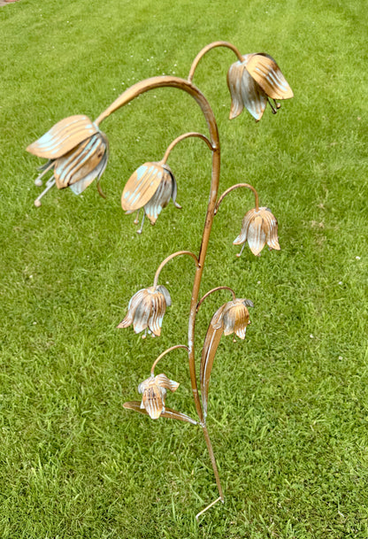 Weathered metal fritillaria ornament displayed among plants in a cottage garden setting