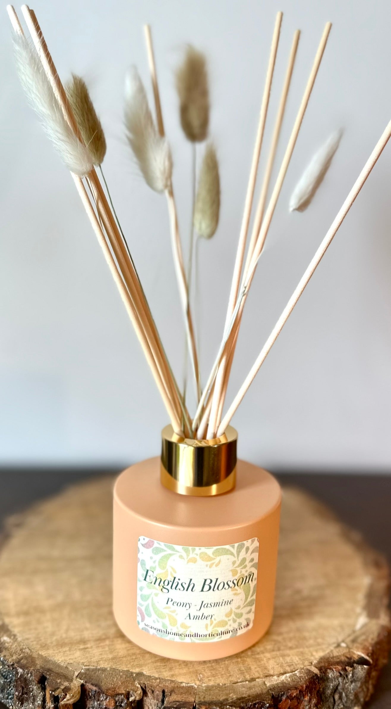 English Blossom reed diffuser with peony, jasmine and amber fragrance in frosted glass bottle with natural reeds on wooden surface