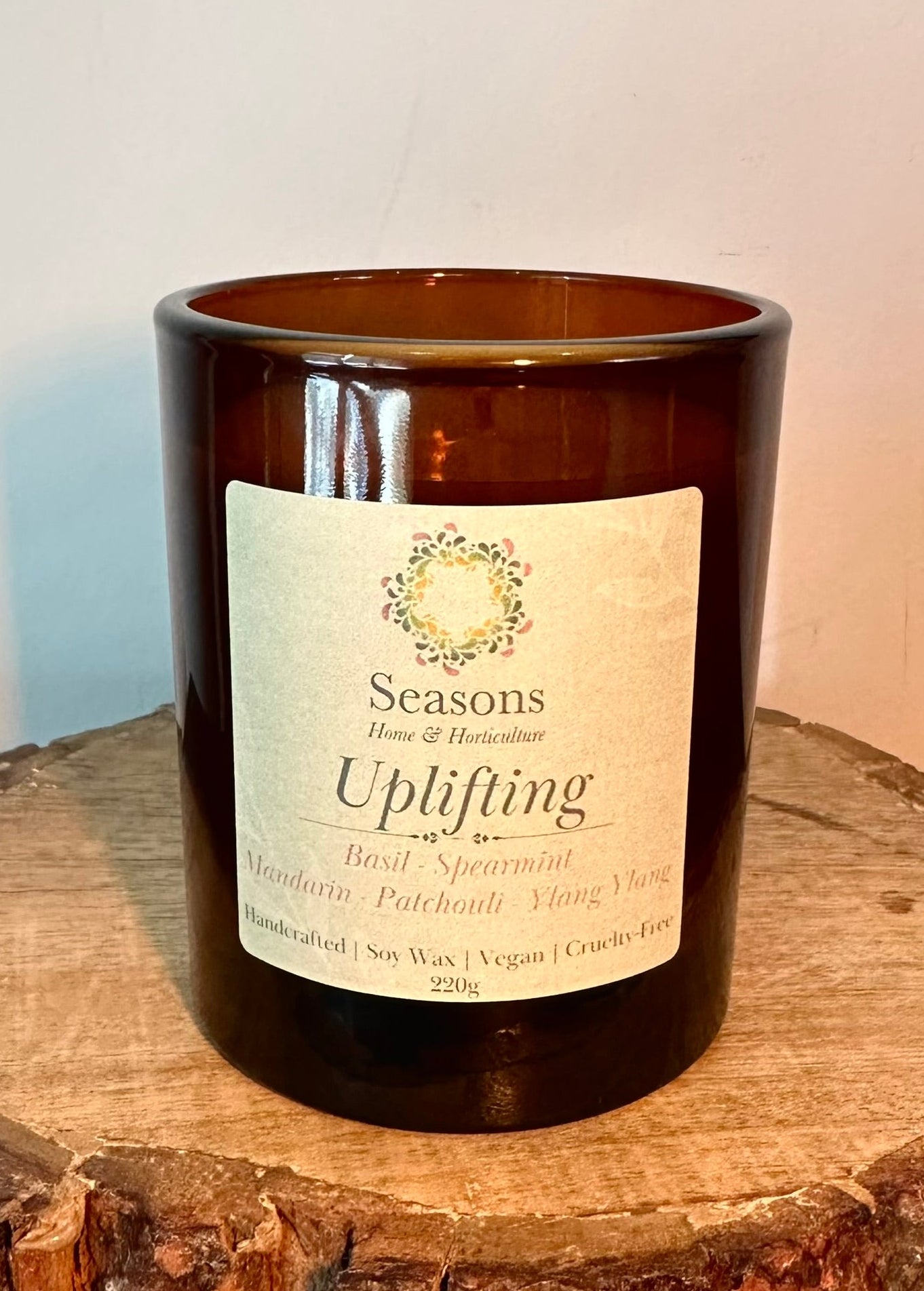 Handmade uplifting scented candle with essential oils in amber jar featuring basil, mint and citrus notes on wooden surface