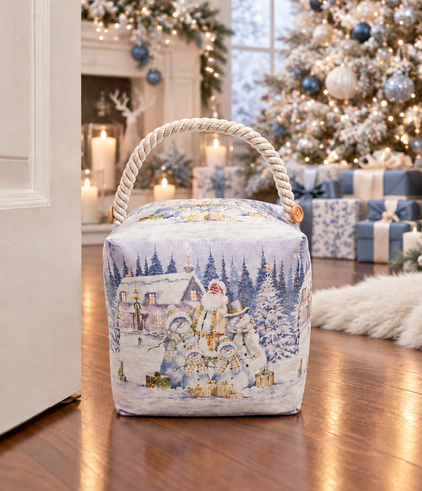A square fabric storage bag with a rope handle, featuring a winter Christmas scene print with Santa, snowmen, and a snowy house. An inset in the top-left shows the bag illuminated with warm lights.