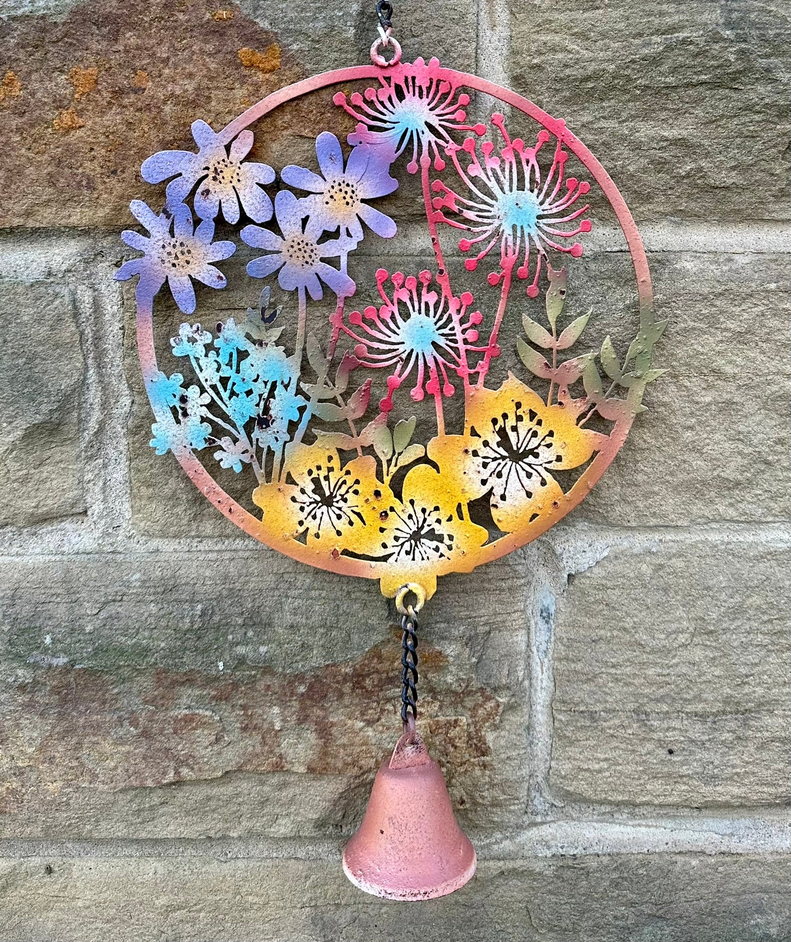 Decorative metal wall art with colourful flowers on a stone wall background