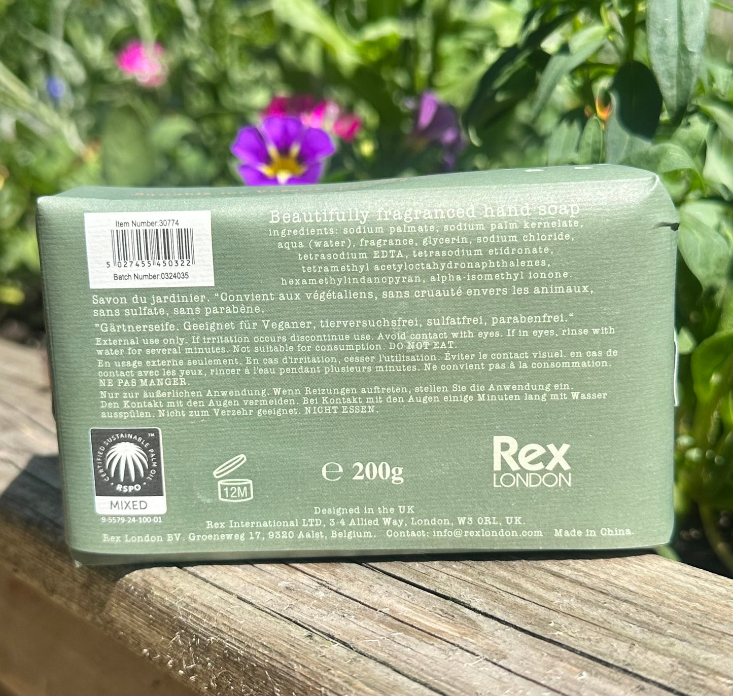 Green soap bar with branding and text on a wooden surface with plants in the background