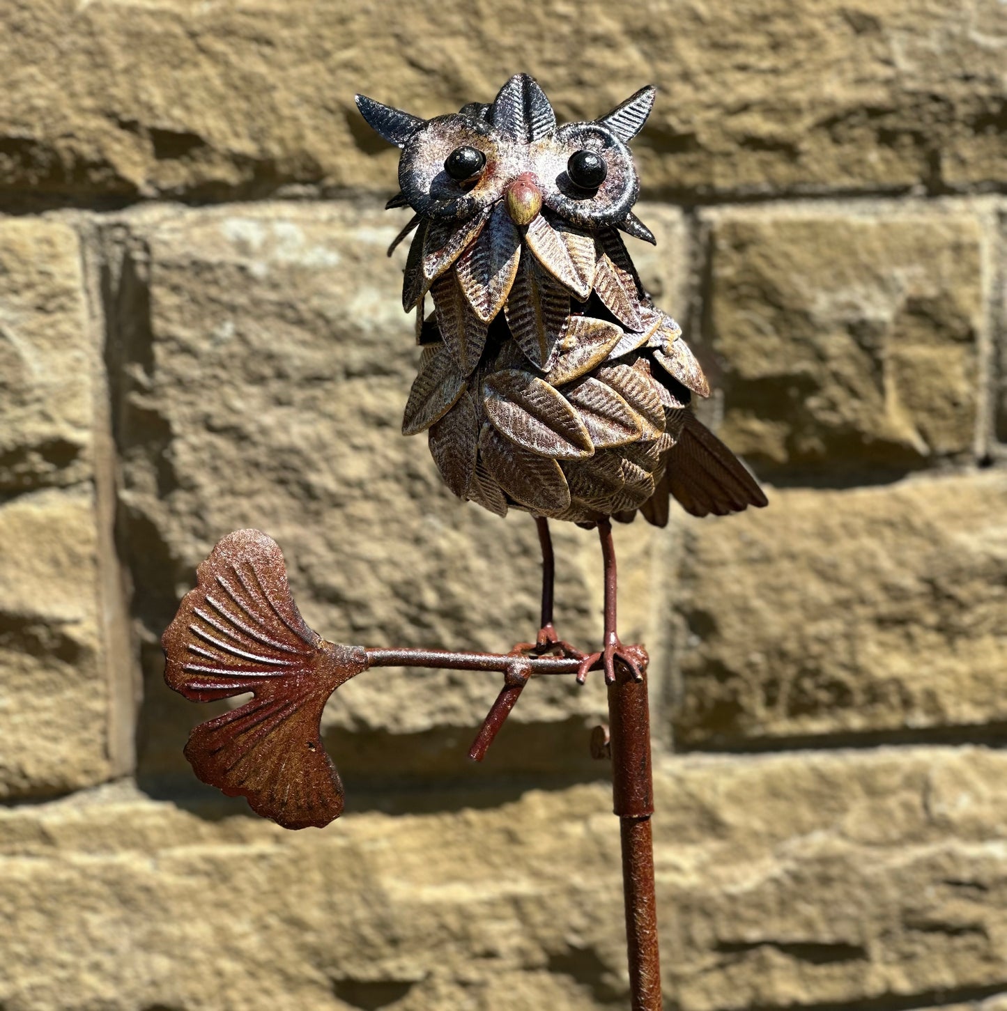 Decorative metal owl stake sculpture on a stone wall background