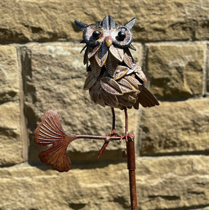 Decorative metal owl stake sculpture on a stone wall background