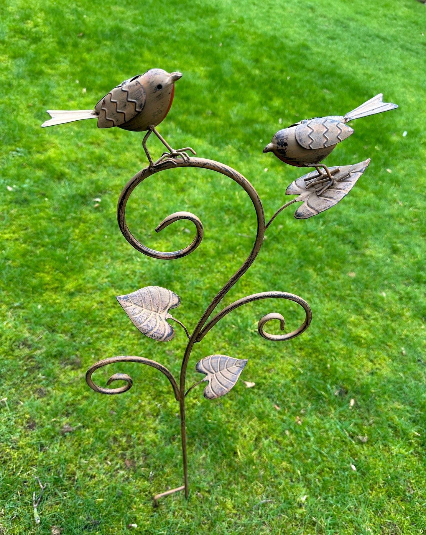 Decorative metal garden stake with birds on a green lawn