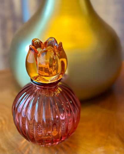 Small pink glass candle holder with a ribbed design and amber-colored tulips style top on a wooden surface.