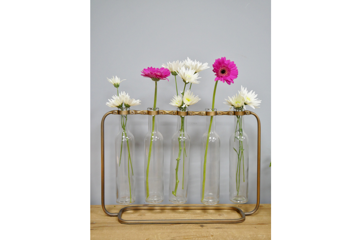Glass bottles with floral arrangements in a metal stand on a wooden surface.