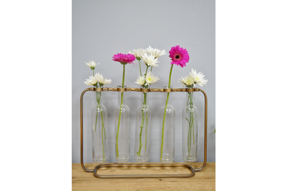 Glass bottles with floral arrangements in a metal stand on a wooden surface.