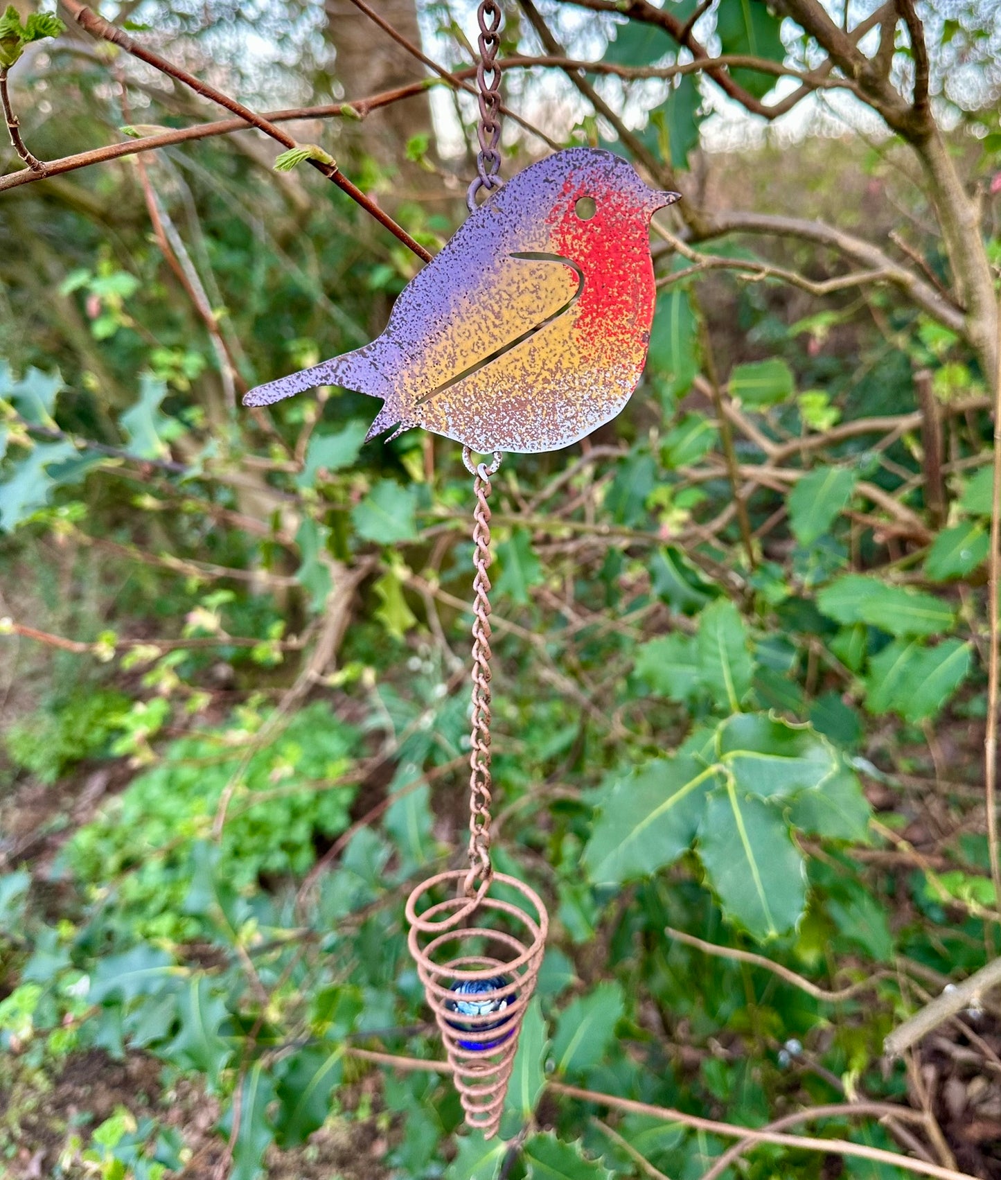 Colorful robin wind chime hanging from a tree branch with a natural green background.