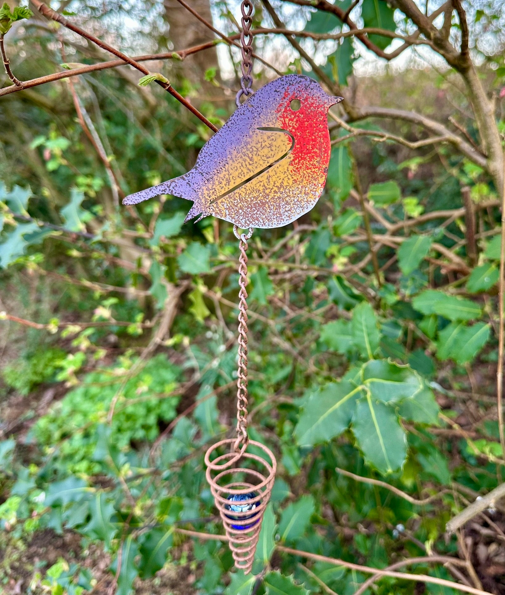 Colorful robin wind chime hanging from a tree branch with a natural green background.