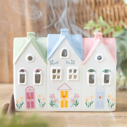 Decorative ceramic house-shaped tealight holder or incense burner with smoke coming out on a wooden surface.