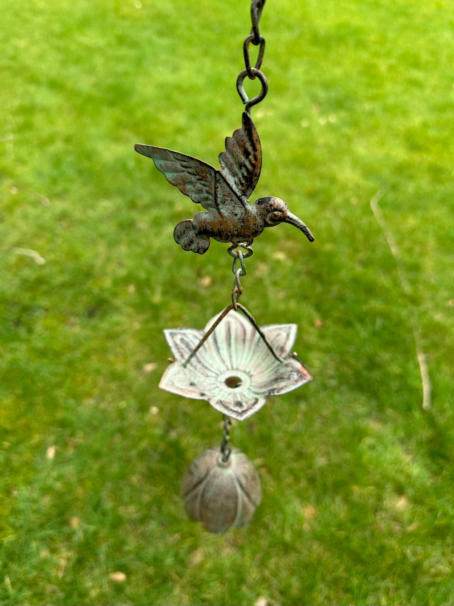 Decorative hanging ornament with a hummingbird design against a green grass background