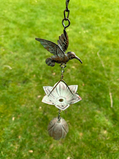 Decorative hanging ornament with a hummingbird design against a green grass background