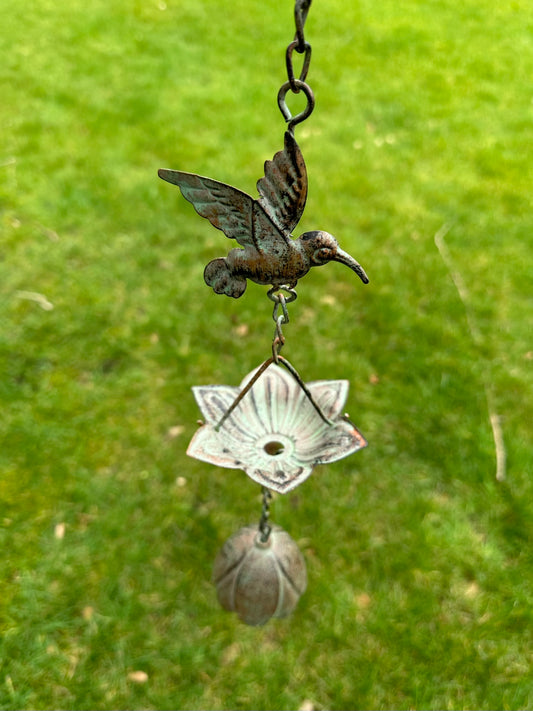 Decorative hanging ornament with a hummingbird design against a green grass background