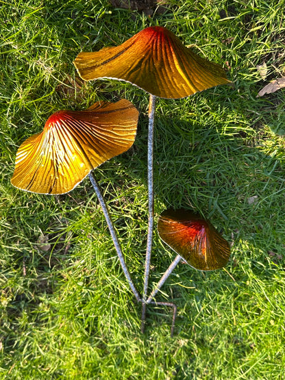 Decorative metallic toadstool ornaments for fairy gardens and outdoor plant displays in rustic garden setting