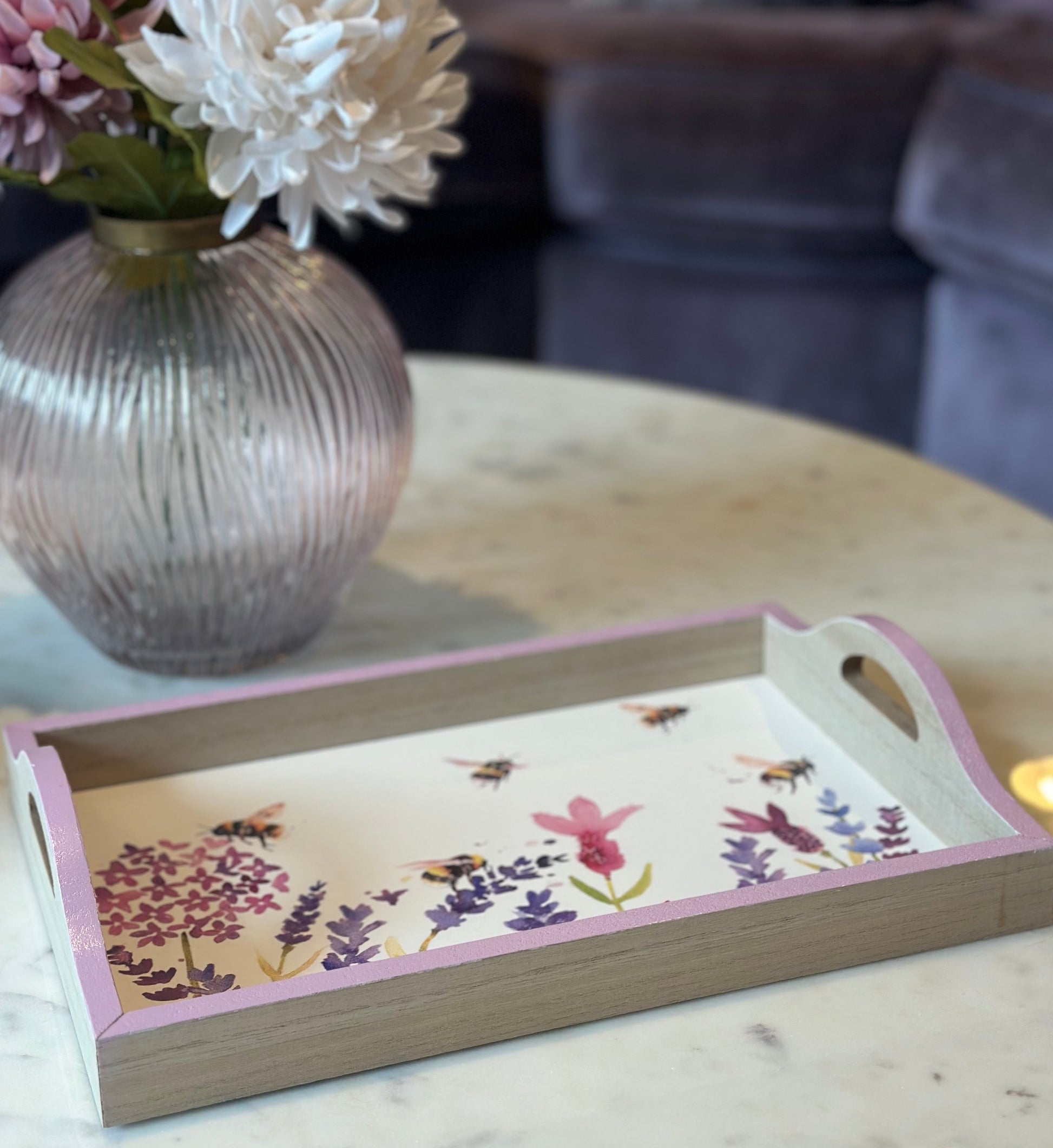 Decorative tray with floral design on a marble surface next to a vase with flowers.