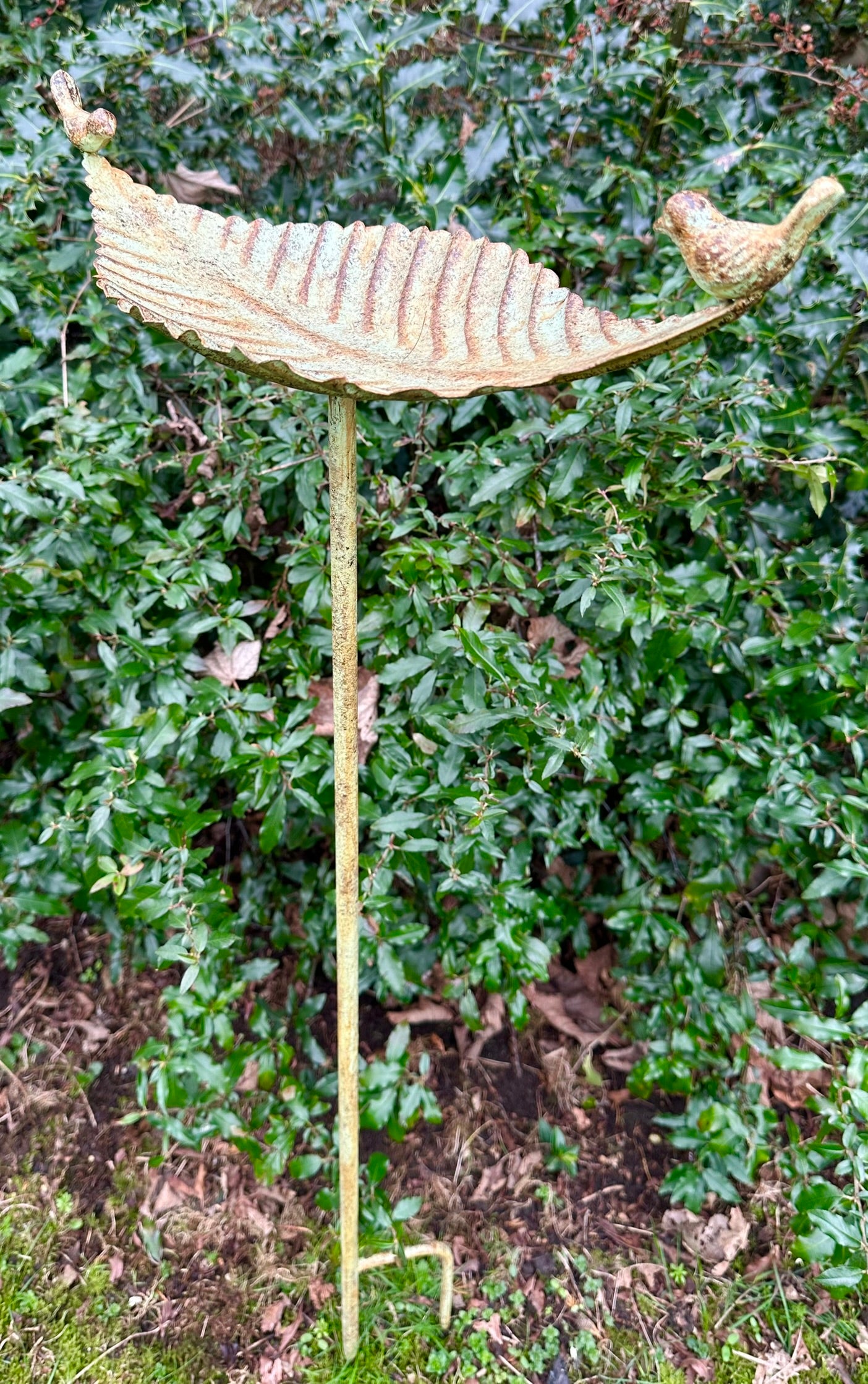 Decorative garden stake with leaf and bird design against a green bush background