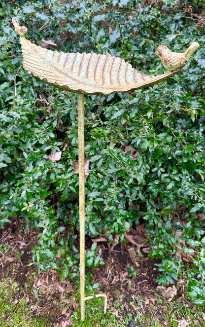 Decorative garden stake with leaf and bird design against a green bush background