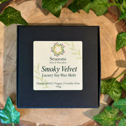 Box of Seasons Smoky Velvet wax melts with a decorative label on a wooden surface with ivy leaves.