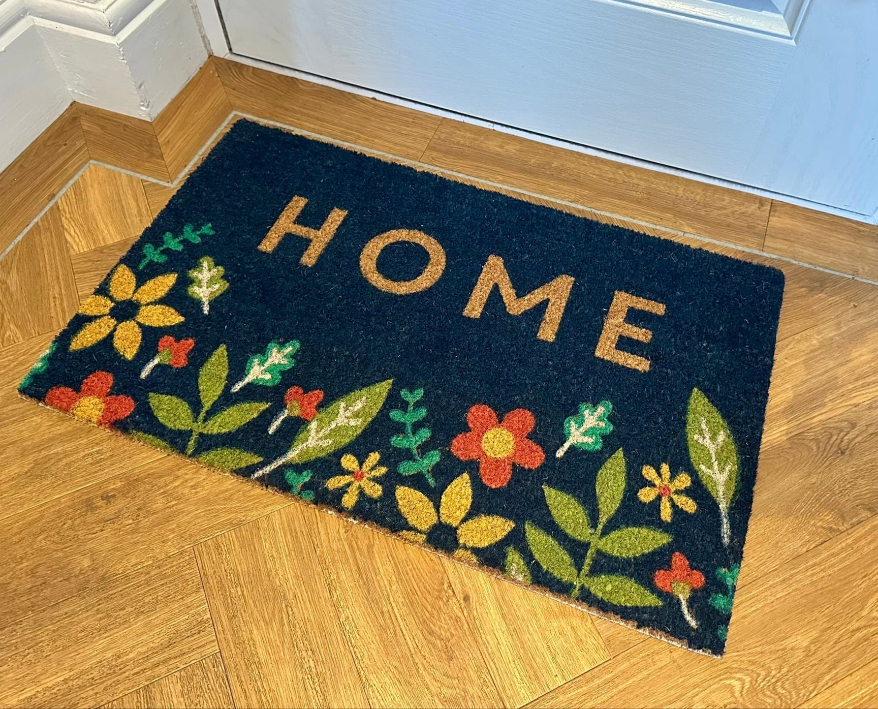 navy blue doormat with the words home printed on, with floral images at the bottom
