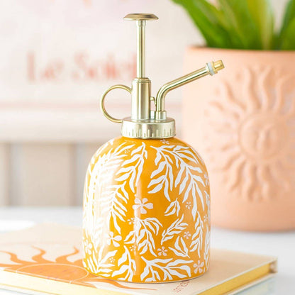 Yellow ceramic spray bottle with white leaf patterns on a surface.