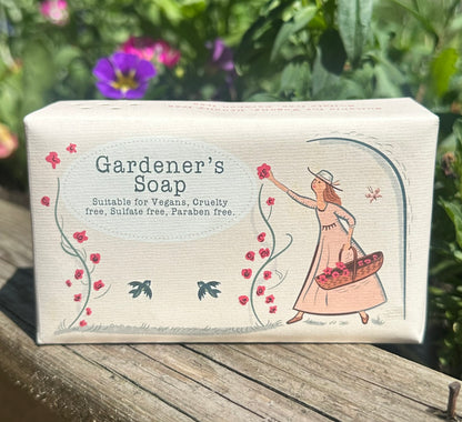 Two bars of Gardener’s Soap with floral and outdoors packaging sitting on a garden planter in summer sunlight

