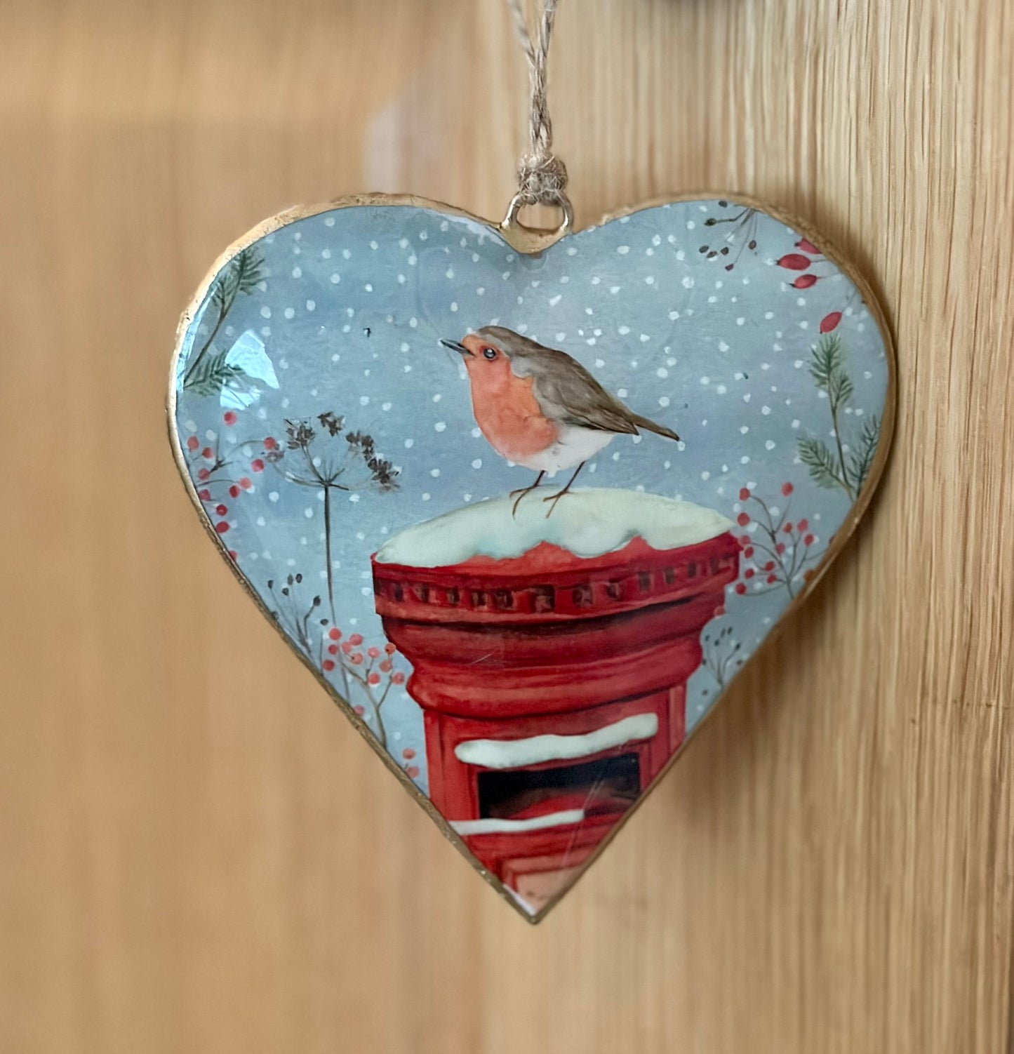 Heart-shaped metal ornament with a robin and postbox design on a wooden background