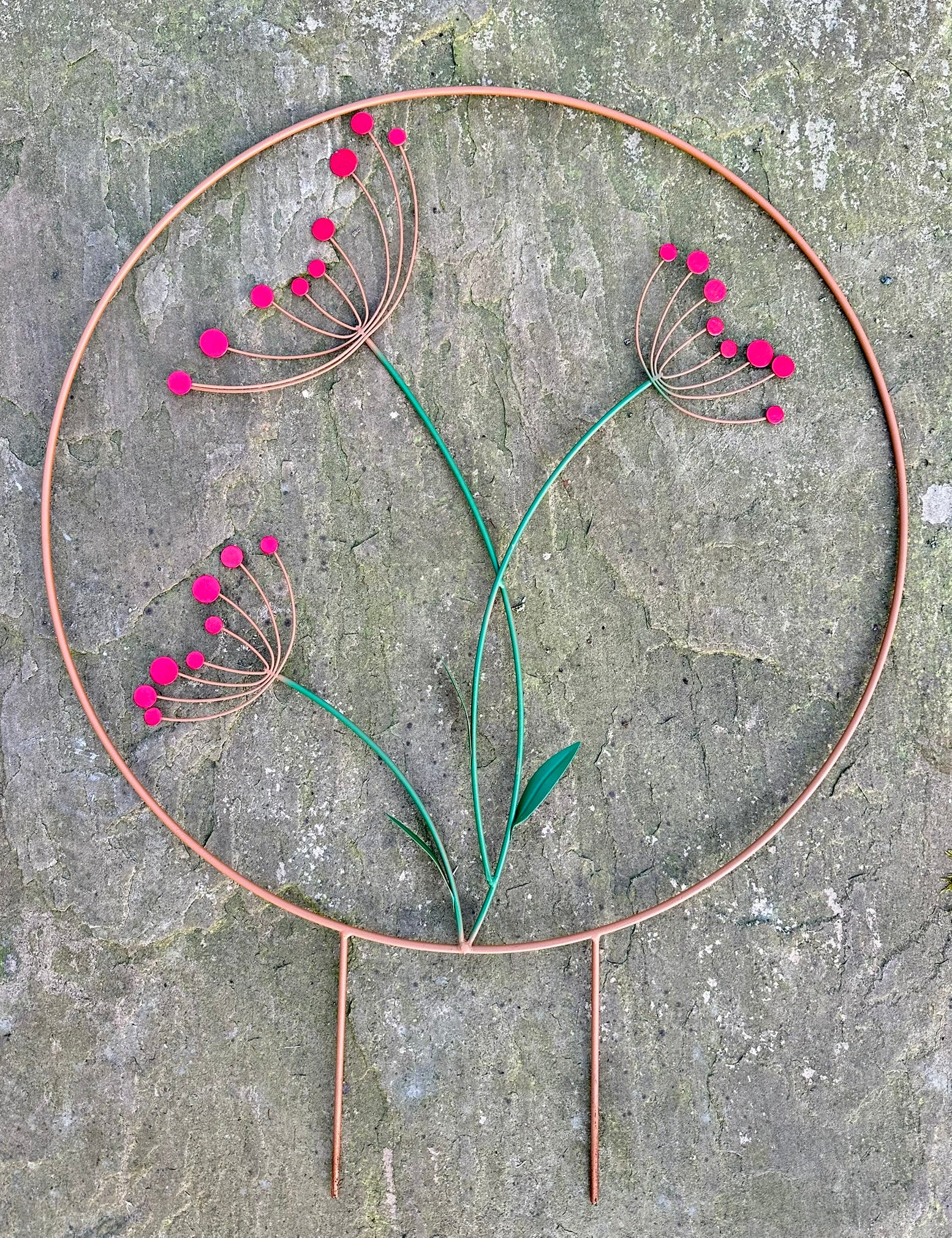 Decorative metal plant stake with red flowers on a stone surface