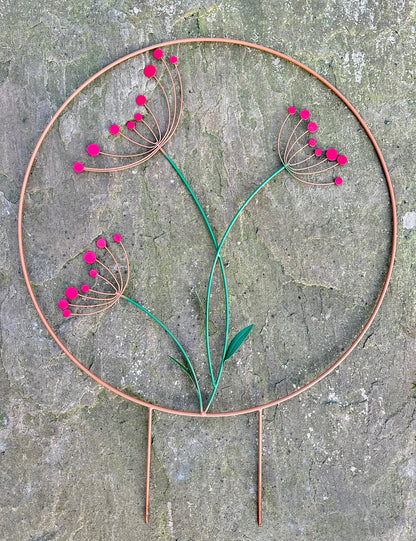 Decorative metal plant stake with red flowers on a stone surface