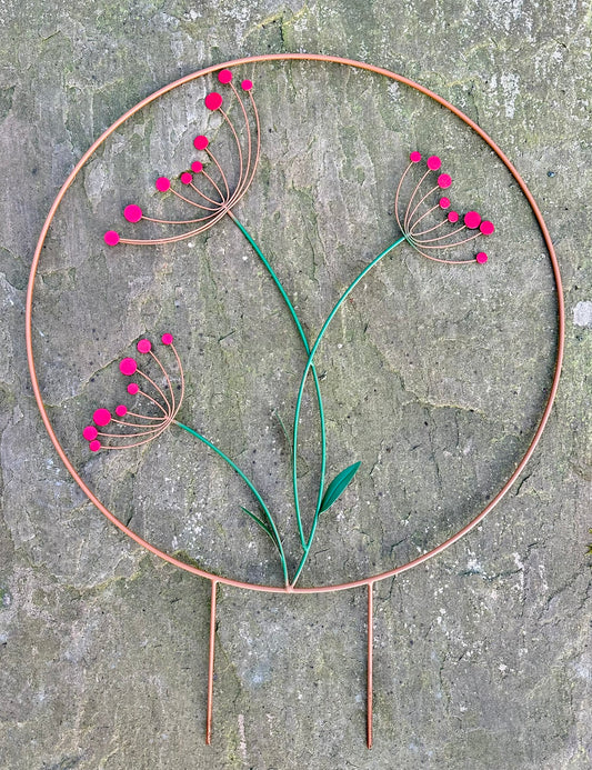 Decorative metal plant stake with red flowers on a stone surface