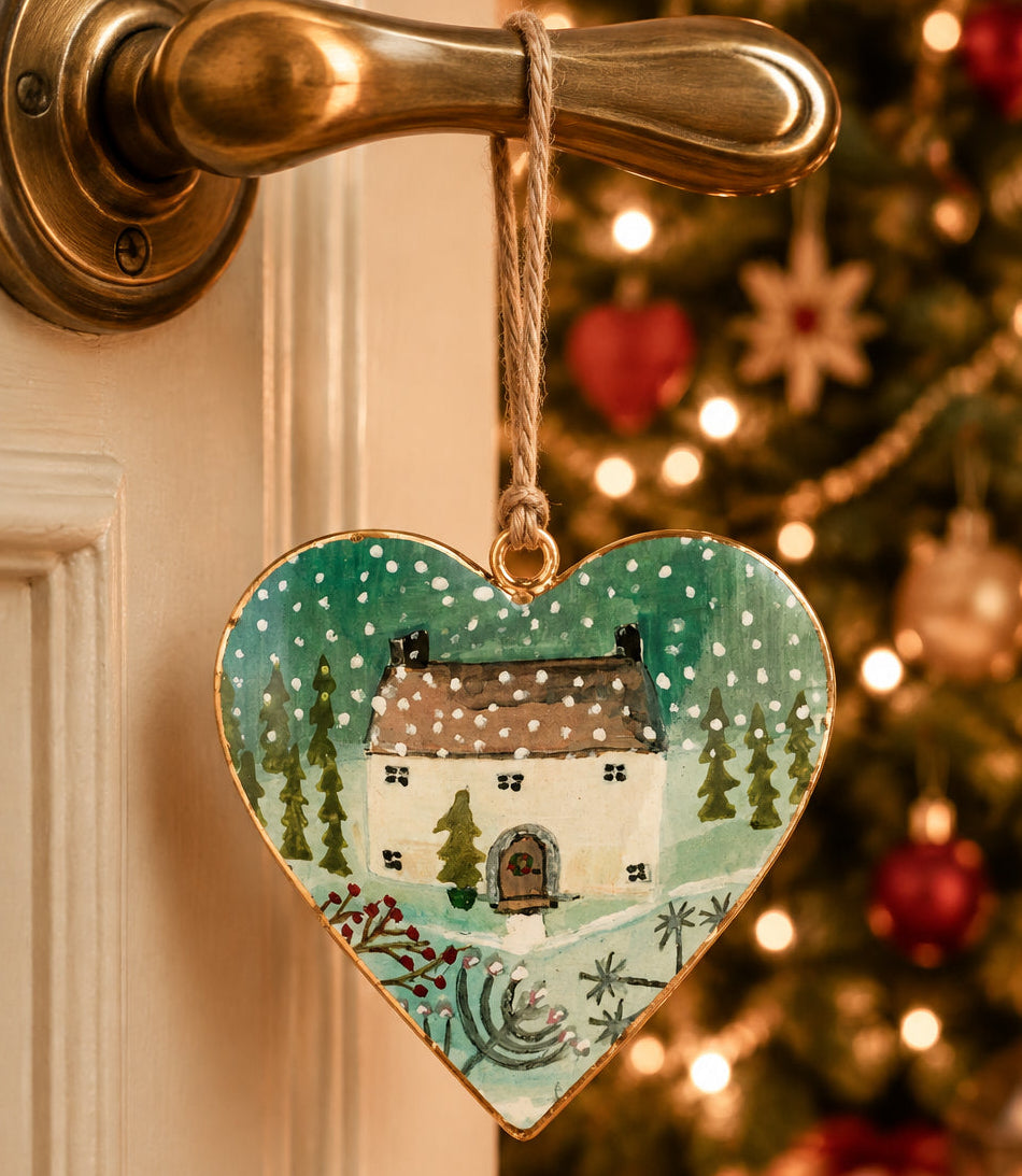 Heart-shaped ornament with a winter scene of a house and trees on a white background
